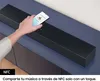 A hand is holding a smartphone over a black soundbar, demonstrating NFC pairing. Voir les images du produit