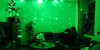A person sits on a couch in a room illuminated by a green star projector. Podgląd zdjęcia produktu