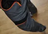 A close-up view of a pair of gray work pants with orange and black accents, resting on a wooden floor. Produktbild-Vorschau