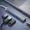 A silver USB hub with four blue USB ports is connected to a laptop, with several USB drives and a wireless adapter placed around it on a gray surface. Produktbild-Vorschau