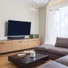 A modern living room with a TV mounted on the wall above a wooden media console. A large sectional sofa is in the foreground. Anteprima dell’immagine prodotto