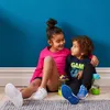 Two children sitting on the floor in front of a blue wall, with water bottles beside them. Náhled obrázku produktu