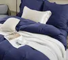 A neatly made bed with navy blue bedding, white throw blanket, and decorative pillows. Produktbild-Vorschau