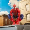 A Spider-Man action figure is posed in a crouching position on top of a ledge, with buildings and a blue sky in the background. Podgląd zdjęcia produktu