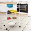 A white metal kitchen trolley filled with fruits and a plate, placed on a tiled kitchen floor in front of a stove. Náhľad obrázku produktu