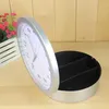 A clock with a hidden compartment is shown open, revealing its storage sections. A potted plant with pink flowers is visible in the background. Voir les images du produit