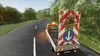A truck carrying a traffic sign with lights is driving on a winding road through a forest. Produktbild-Vorschau