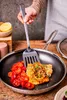 A person is using a spatula to flip a piece of fish in a frying pan with cherry tomatoes. Náhled obrázku produktu