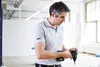 A man is holding a cordless drill in a workshop or construction setting. Voir les images du produit