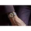 A close-up shot of a man's wrist wearing a watch, with his suit jacket and trousers visible. Voir les images du produit