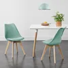 Two mint green dining chairs with wooden legs are placed around a white dining table. A potted plant and some plates are on the table. A light blue pendant lamp hangs above. Náhled obrázku produktu