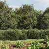 A wire mesh fence in a garden setting, with plants and trees in the background. Náhľad obrázku produktu