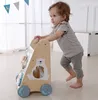 A baby is using a wooden walker with colorful blocks and animal figures. Náhled obrázku produktu