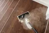 A steam cleaner is being used to clean a wooden floor with visible footprints. Voir les images du produit