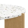 A close-up view of the edge of a round table with a terrazzo-like pattern on its surface and wooden legs. Voir les images du produit