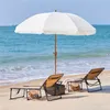 Two lounge chairs and a beach umbrella on a sandy beach with the ocean in the background. Produktbild-Vorschau