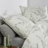 A close-up view of bedding with a floral pattern, including pillows and a duvet cover, with two green candles in the foreground. Produktbild-Vorschau