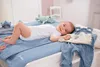 A baby lying on a changing mat with baby clothes and toys. Produktbild-Vorschau
