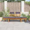 A wooden garden bench with gray cushions is placed on a paved patio in front of a wooden fence. Náhľad obrázku produktu
