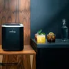 A black LEHMANN ice maker sits on a wooden cabinet next to two cocktails and a decanter of liquid. Náhled obrázku produktu