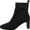A black knitted ankle boot with a block heel and a patterned design is shown against a white background. Produktbild-Vorschau