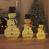 Three illuminated snowmen of varying sizes are displayed indoors, decorated for Christmas with a Christmas tree and fireplace in the background. Náhled obrázku produktu