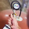 A hand holding a device with a pressure gauge attached to a large, round, brown object. Produktbild-Vorschau