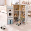 A wooden police and fire station playset with toy vehicles and figures on a pink leaf-patterned rug, with a crib and clothing rack in the background. Anteprima dell’immagine prodotto