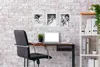 A home office setup with a desk, chair, laptop, and framed pictures on a brick wall. Náhľad obrázku produktu