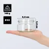 A hand holding a small glass jar with dimensions and weight indicated. Produktbild-Vorschau