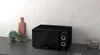 A black microwave oven is placed on a kitchen counter next to a cutting board and a potted plant. Anteprima dell’immagine prodotto