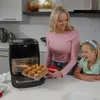 A woman and a child are in a kitchen, with the woman holding a tray of muffins next to an air fryer. Produktbild-Vorschau