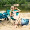 A woman sits on a beach chair with a bottle of drink, next to a beach wagon and a striped tote bag. Náhľad obrázku produktu