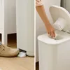 A split image showing a white diaper pail. The left side shows a foot stepping on a pedal to open the pail. The right side shows a hand placing a diaper into the open pail. Produktbild-Vorschau
