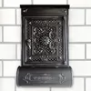 A black mailbox with ornate detailing is mounted on a white brick wall. Produktbild-Vorschau