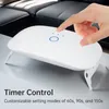 A hand is shown pressing a button on a white UV lamp, which is placed on a table in front of a couch. Produktbild-Vorschau