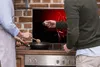 Two people are in a kitchen, one is cooking on a stove while the other is adding seasoning to the pan. The background shows a decorative panel with chili peppers. Náhled obrázku produktu