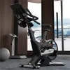 A stationary exercise bike in a modern gym setting with large windows overlooking a city. Náhled obrázku produktu