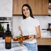 A woman is holding a plate of food in a kitchen, with a bottle of Lea & Perrins sauce on the counter. Podgląd zdjęcia produktu