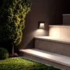 An outdoor stairway with a wall-mounted light illuminating the steps and a tree and grass in the foreground. Produktbild-Vorschau