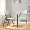 A white folding chair and part of a folding table are set up in a room. Podgląd zdjęcia produktu