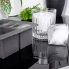A close-up shot of a gray silicone ice cube tray with ice cubes, a glass with ice cubes, and a single ice cube on a reflective black surface. Podgląd zdjęcia produktu