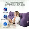 A woman is sitting and reading a book, leaning against a large purple wedge pillow. Produktbild-Vorschau
