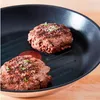Two cooked hamburger patties are in a black grill pan. Produktbild-Vorschau