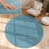 A round blue rug is placed on a wooden floor in a living room setting, with a chair and a pouf nearby. Produktbild-Vorschau