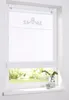 A white Roman blind with a silver crown motif is shown hanging in a window. The lower part of the blind is raised, revealing a view of green foliage outside. A glass vase with greenery and a small candle holder are on the windowsill. Produktbild-Vorschau