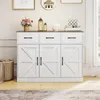 A white buffet cabinet with a brown top, featuring three drawers and three cabinet doors with a barn door design, is displayed in a well-lit room with decorative items on top. Podgląd zdjęcia produktu
