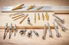 A collection of drill bits laid out on a wooden surface and a metal bar. Produktbild-Vorschau