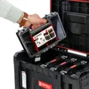 A hand is holding a clear organizer box with red dividers, which is being placed into a larger black tool box. Náhled obrázku produktu