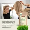 A woman looking in a mirror while a package of Achterhof Gerstengras Pulver is shown in the foreground. Produktbild-Vorschau
